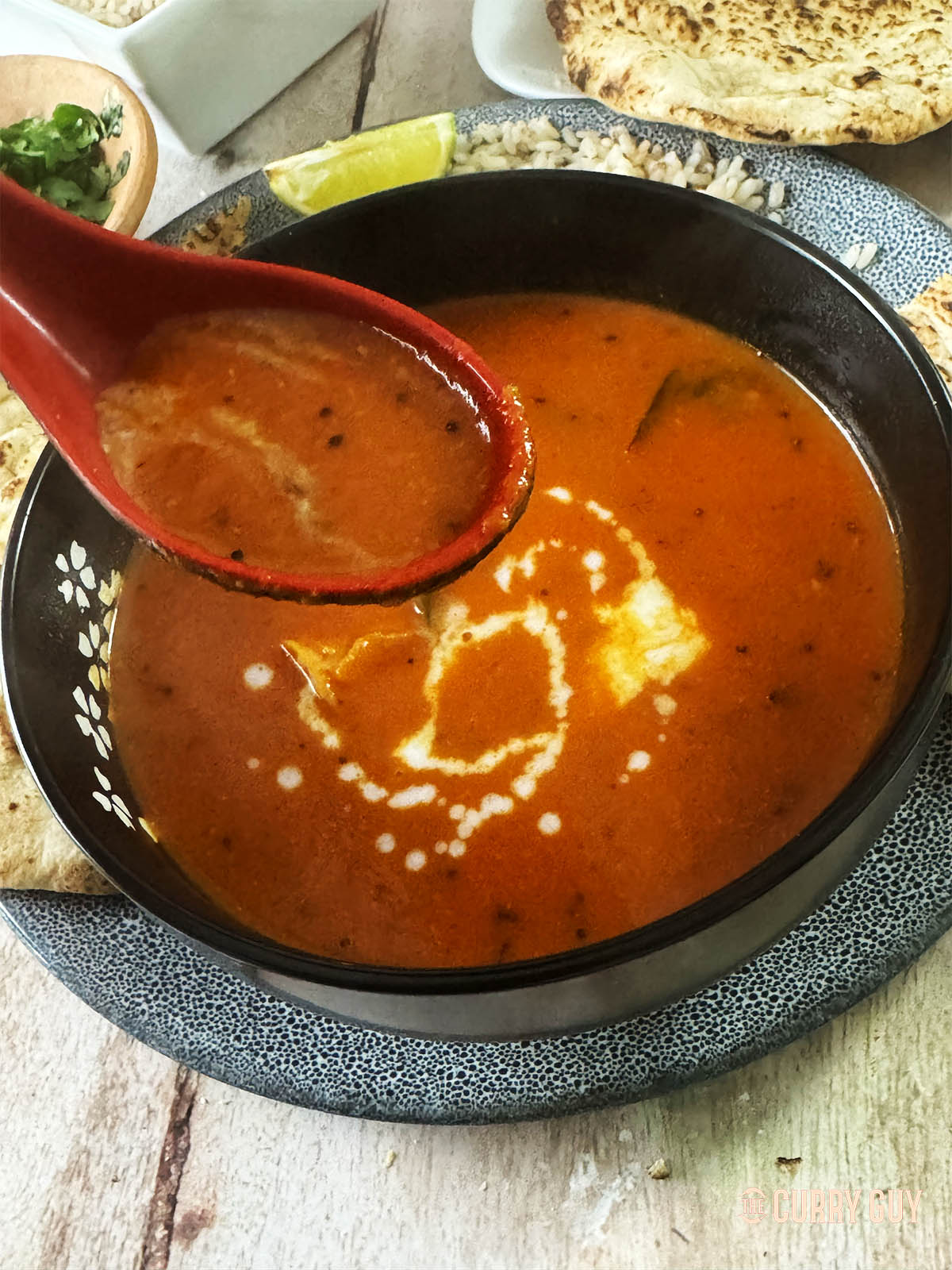 A spoonful of the soup, with the bowl of soup in the background, drizzled with coconut milk. 