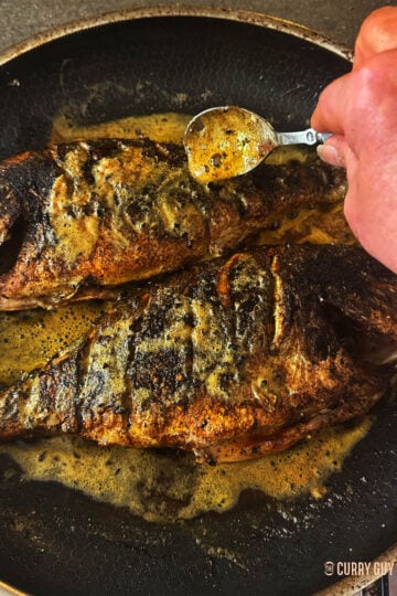 Basting the fish with the butter in the pan.