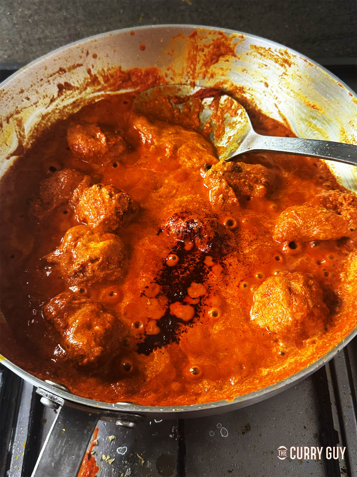 Adding red food colouring and kasoori methi to the pan.