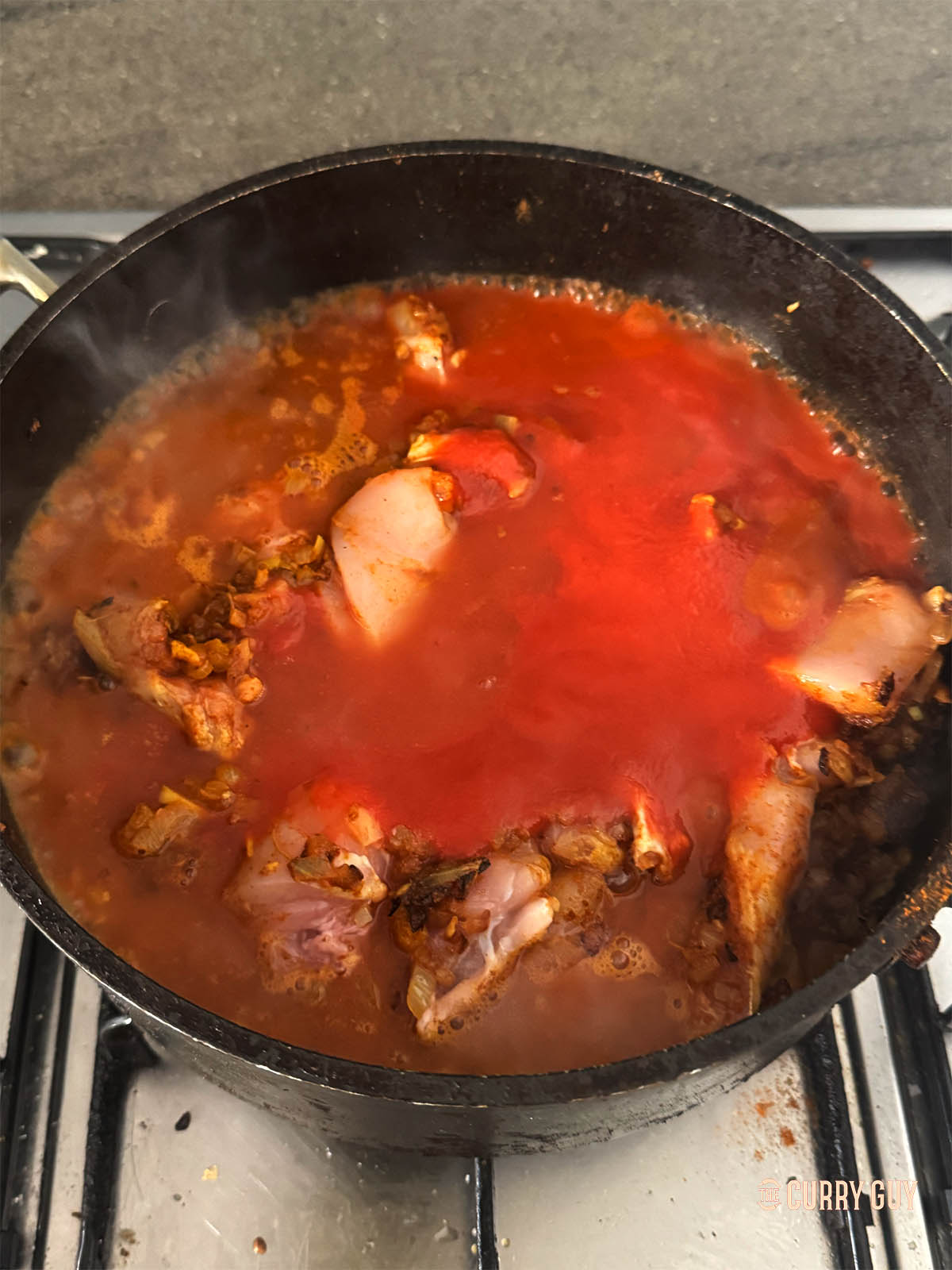 Adding passata to the mixture in the pan with the stock and bringing to a simmer.