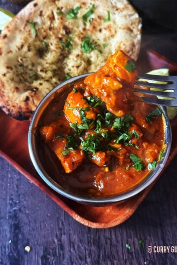 Chicken curry in a serving bowl next to a naan.