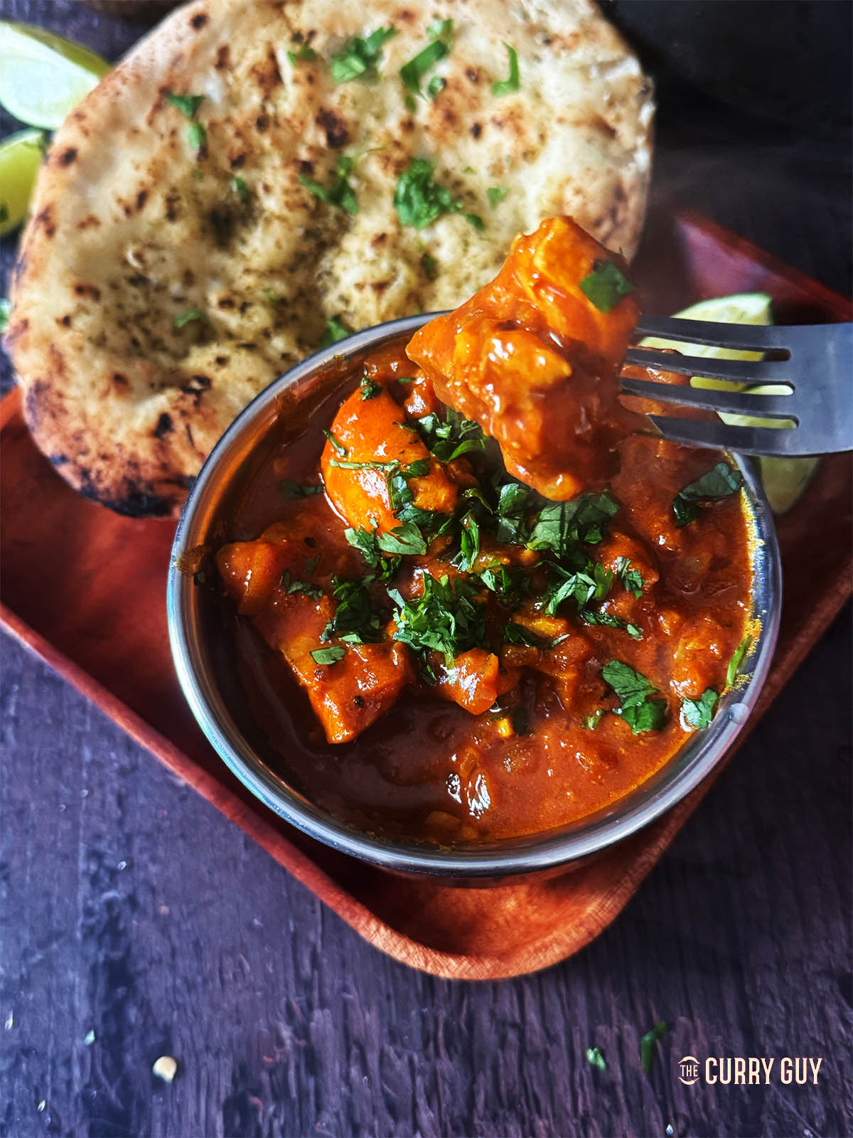 Chicken curry in a serving bowl next to a naan.