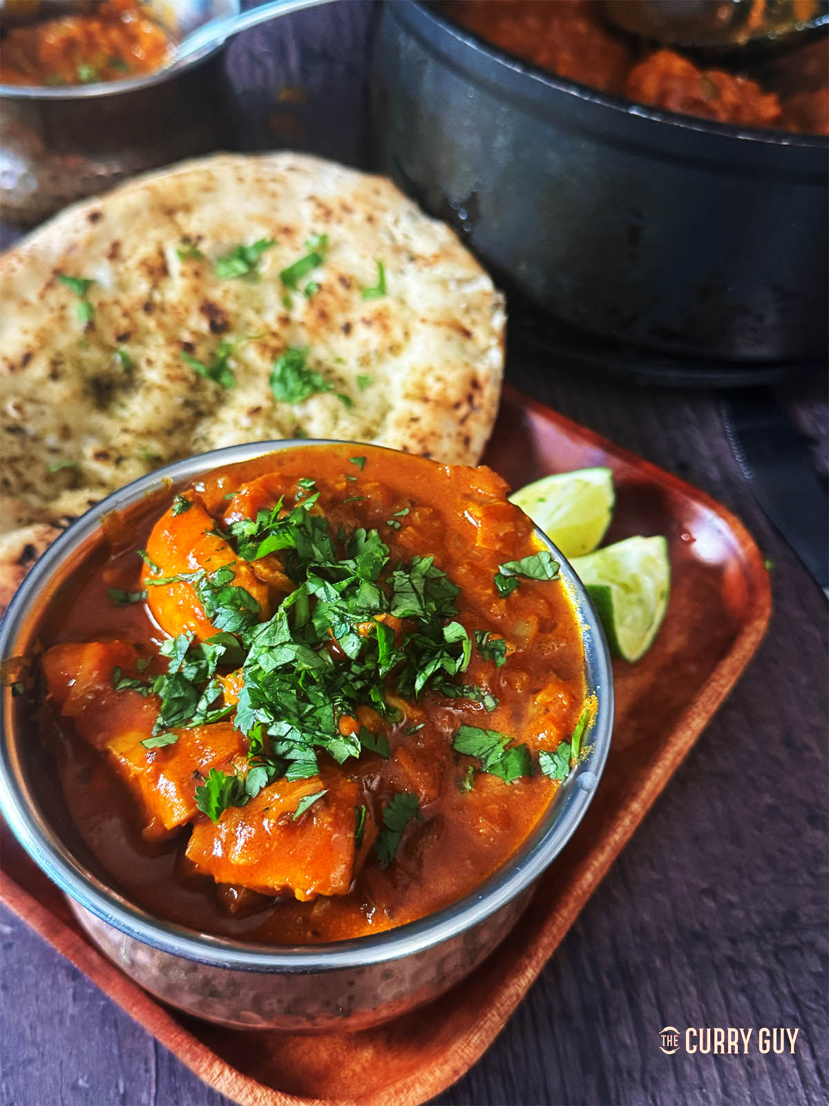 Chicken curry in a serving bowl next to a naan.