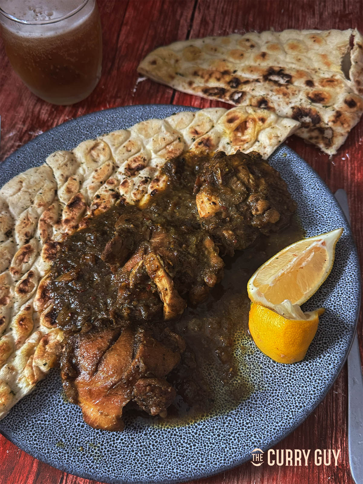 Black chicken curry on a serving plate with a naan and lemon wedges.