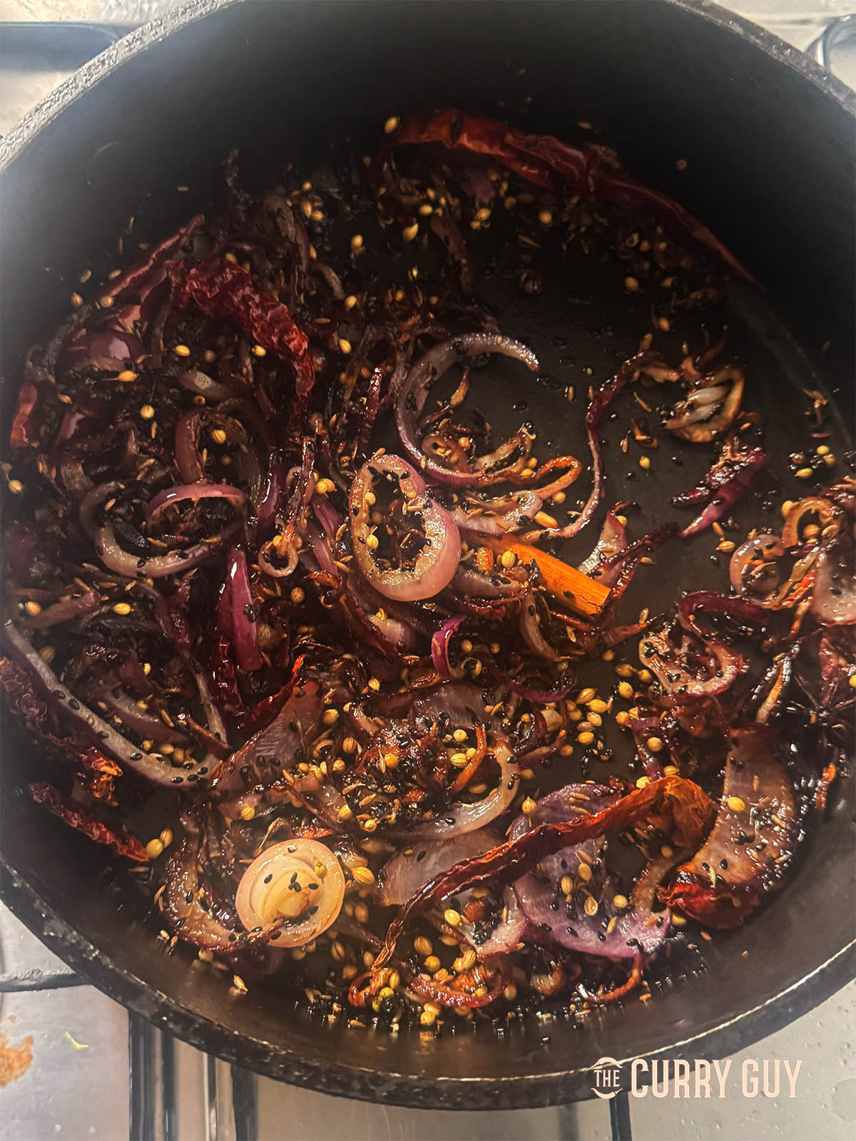 Adding the toasted sesame seeds and whole spices to the fried onions.