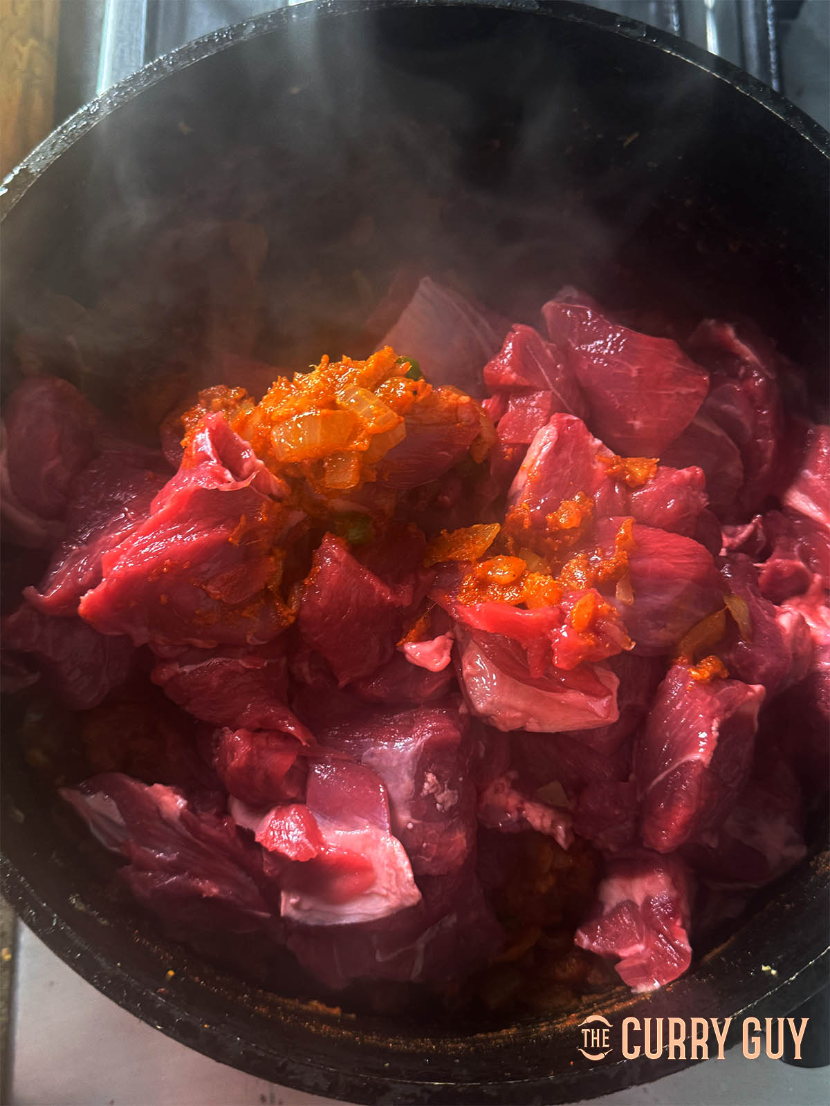 Adding the lamb chunks to the pan to sear them.
