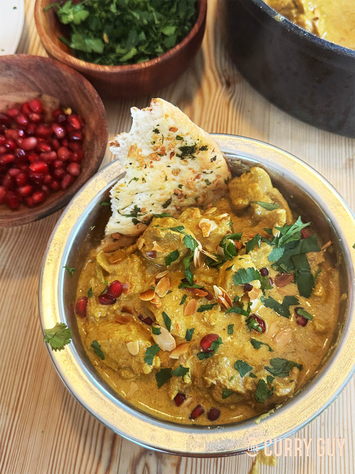 Chicken anarkali in a serving bowl garnished with flaked almonds, pomegranate seeds and coriander.