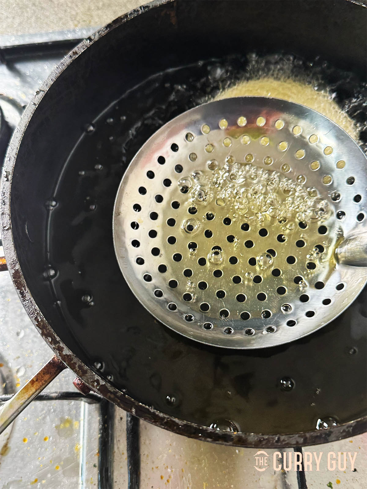 Adding a puri to the hot oil and gently pushing it down with a slotted spoon.