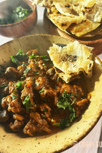 Khatta lamb curry on a serving plate with flatbread and coriander garnish.
