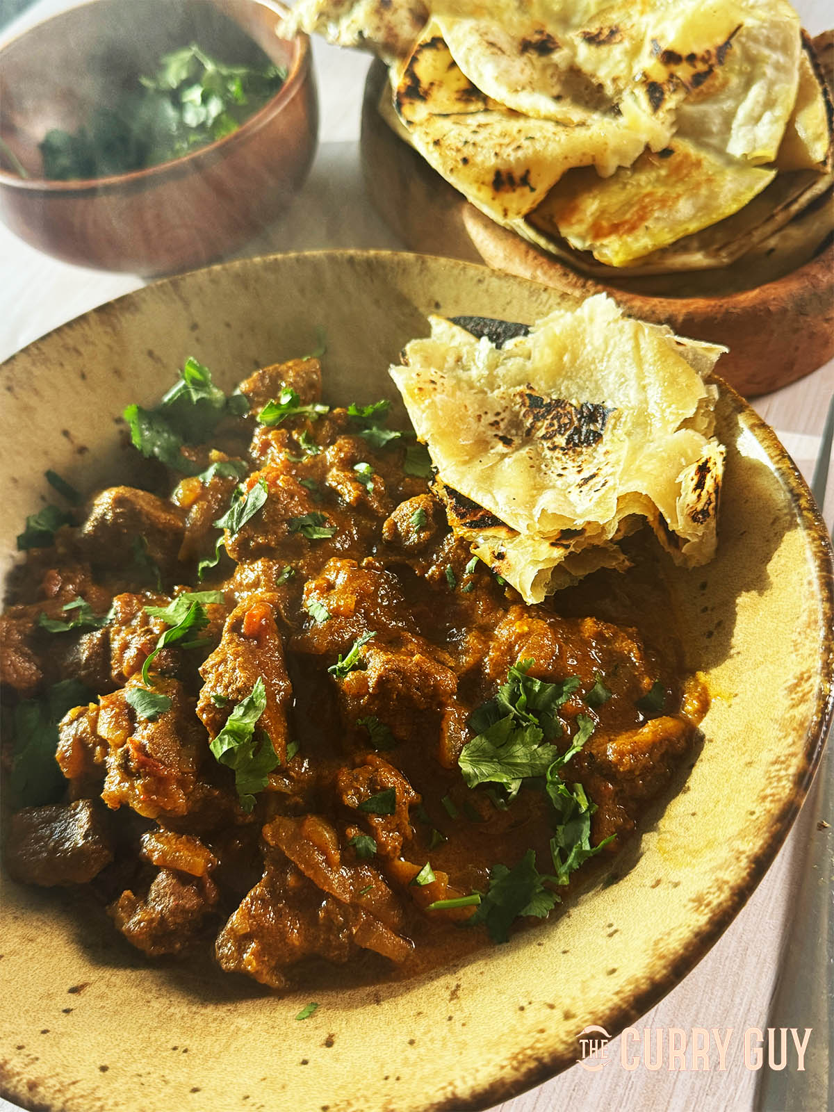 Khatta lamb curry on a serving plate with flatbread and coriander garnish.