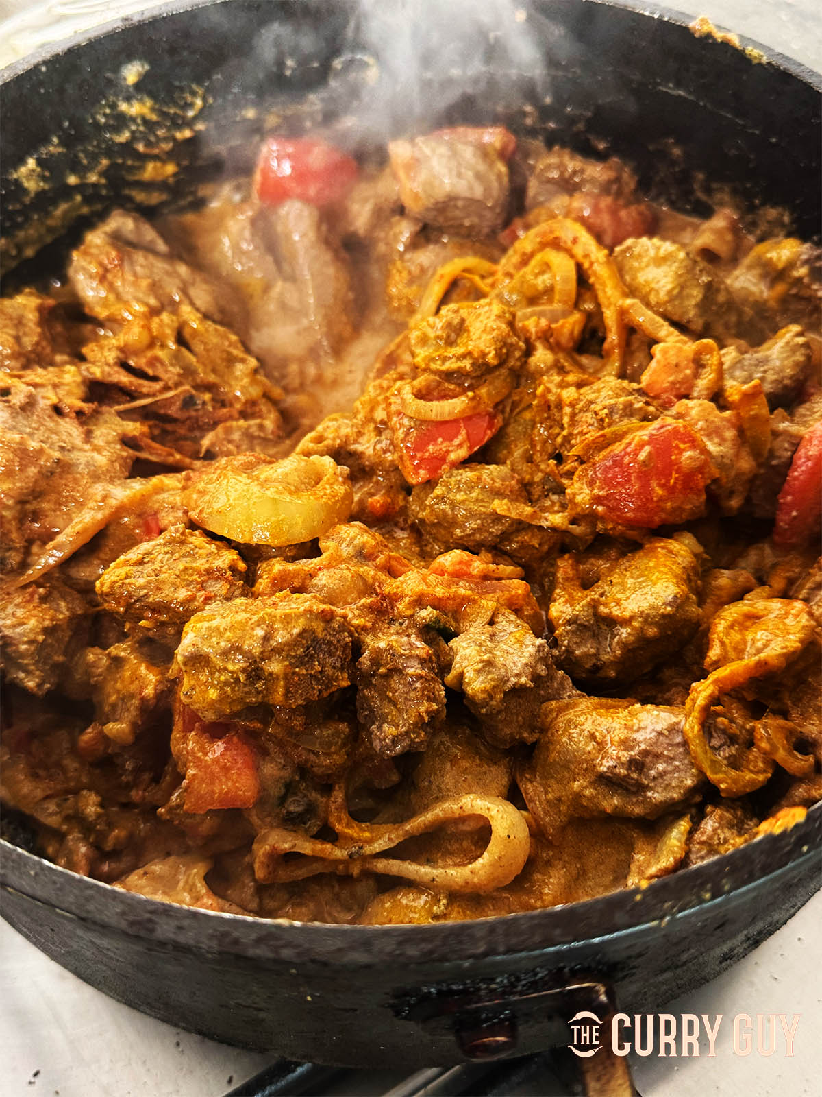 Returning the par-cooked meat to the pan and stirring it into the base masala.