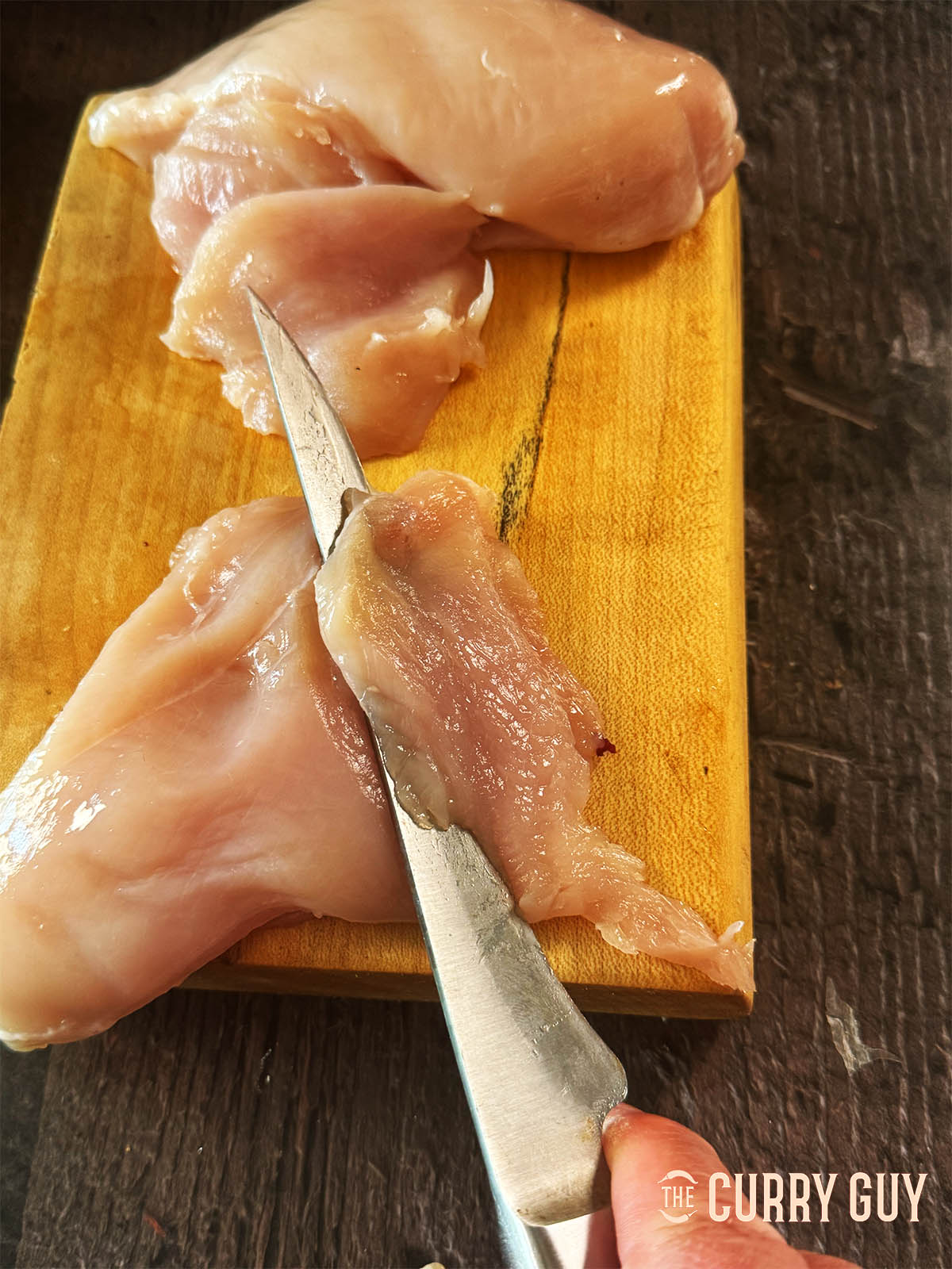 Slicing the chicken against the grain into thin pieces.