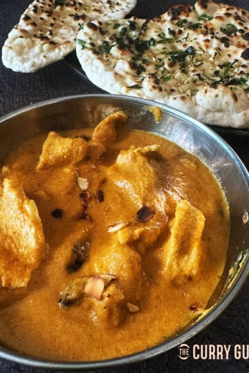 Chicken Pasanda curry in a serving bowl next to naans.