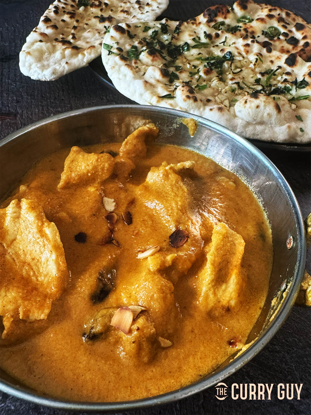 Chicken Pasanda curry in a serving bowl next to naans.
