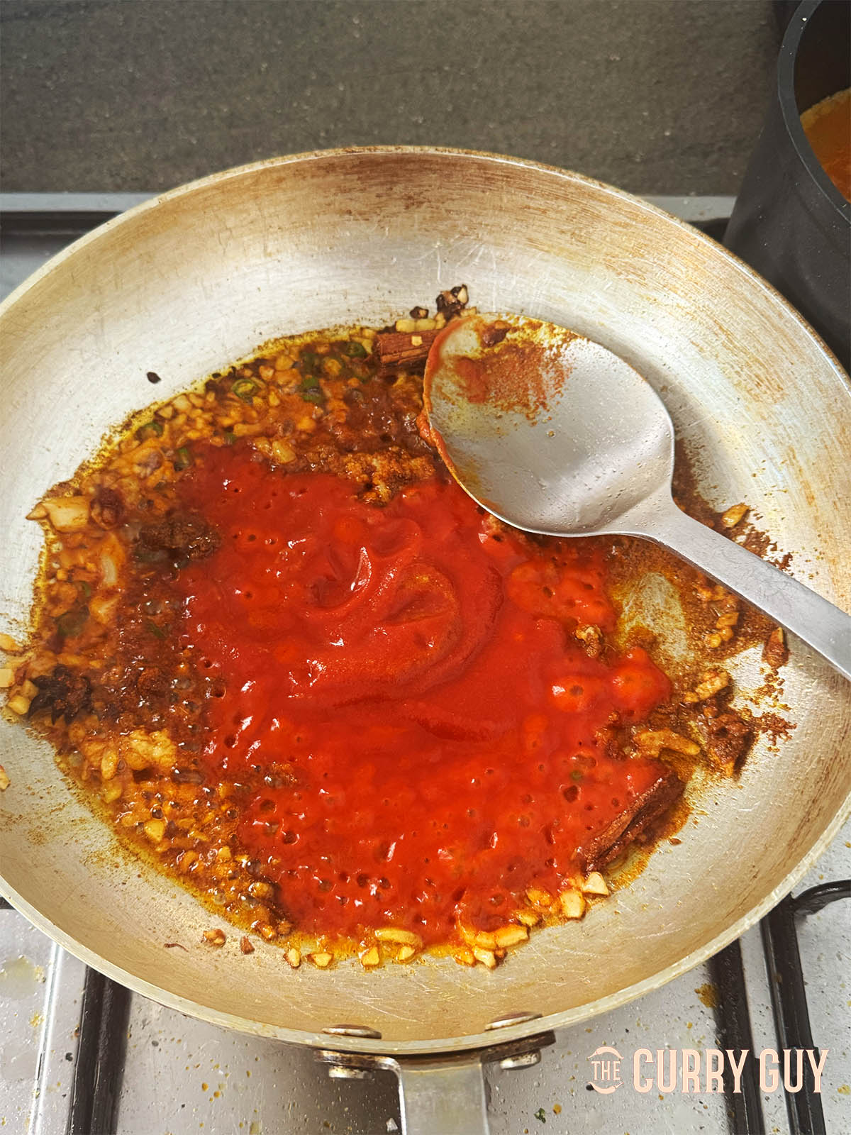 Adding the passata to the pan and bringing to a simmer.
