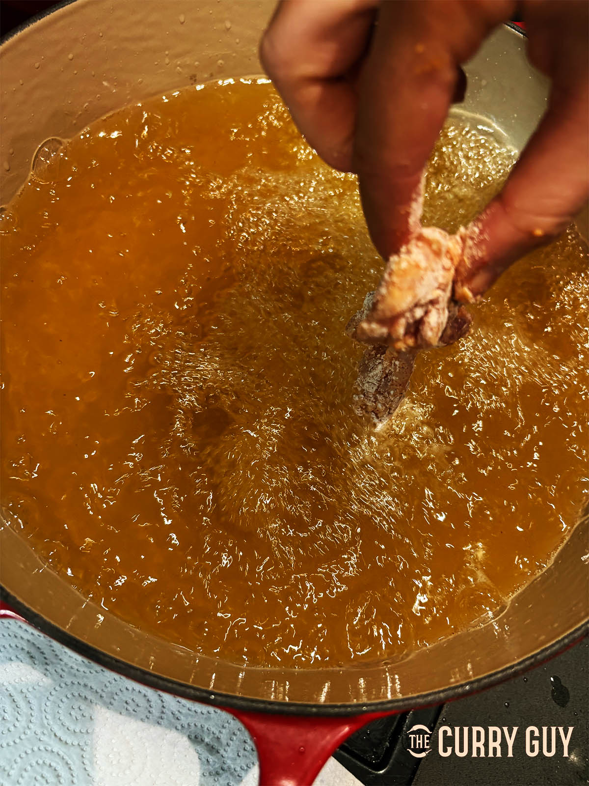 Lowering a piece of chicken into the hot oil.