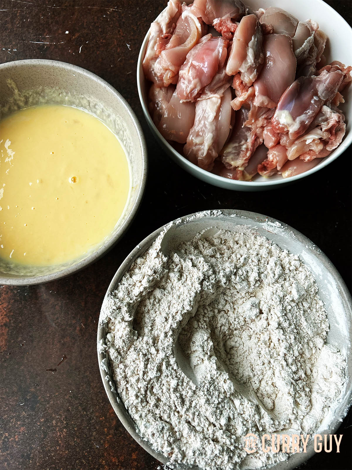 A bowl of the flour mixture and a bowl with eggs and buttermilk next to the chicken to be fried.