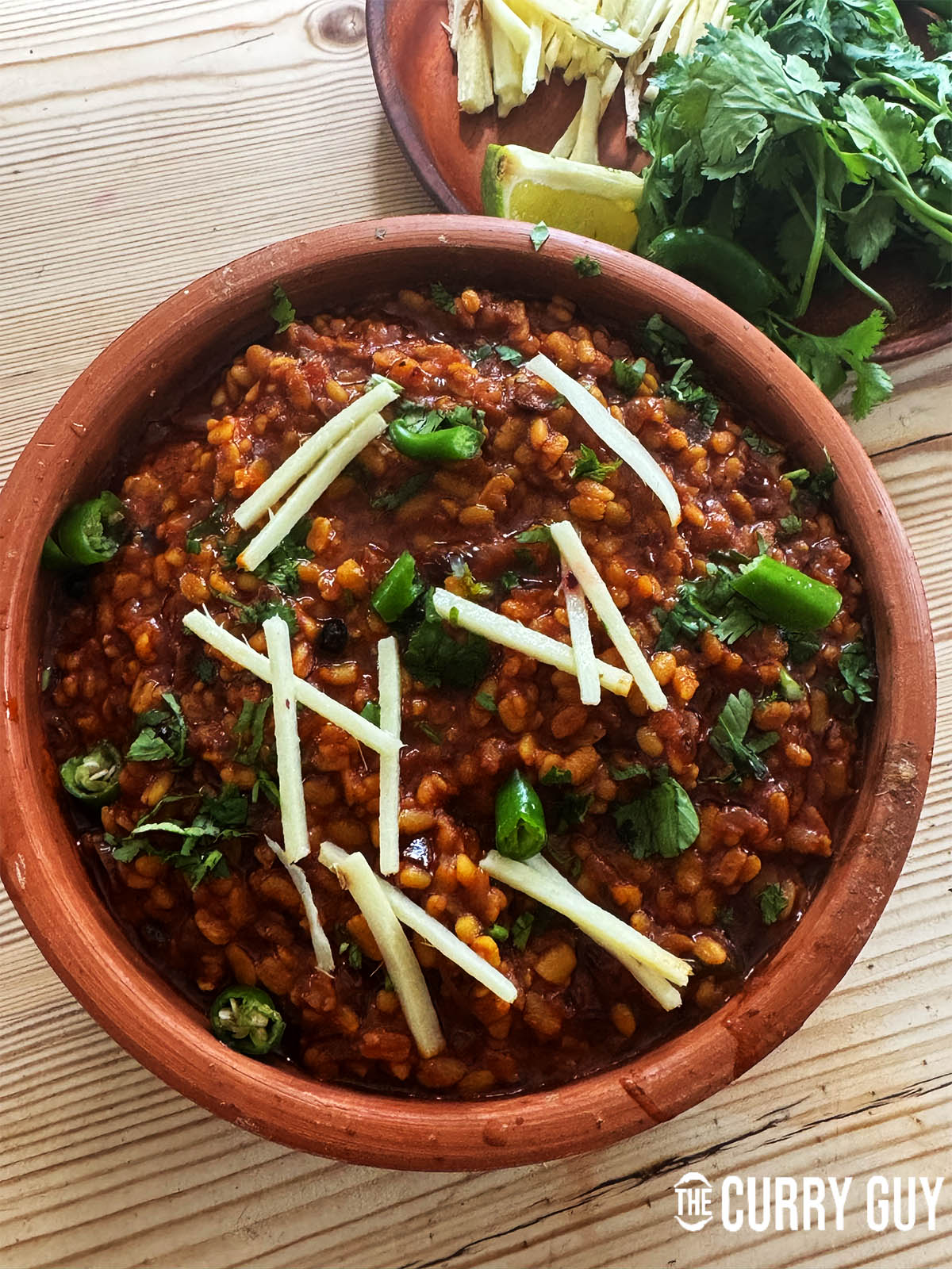 Daal Mash in a serving bowl garnished with julienned ginger, chopped chillies and coriander.