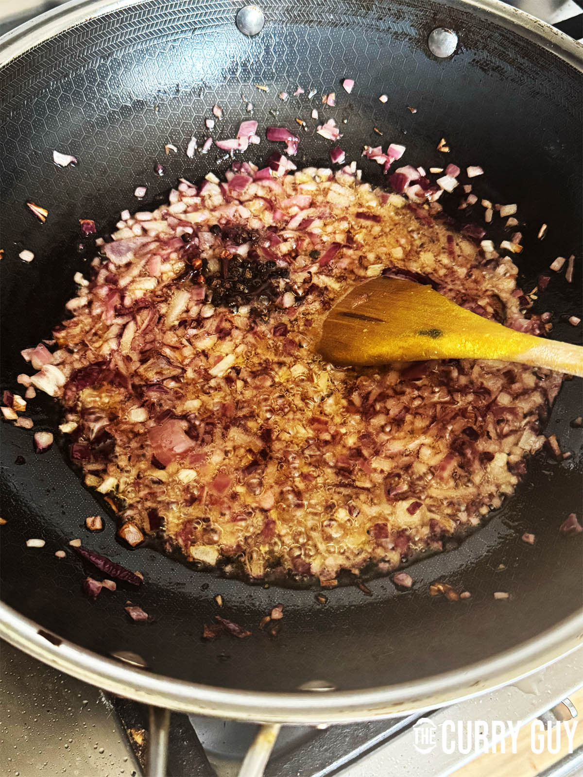 Frying the chopped onions and whole spices in hot ghee in another pan.