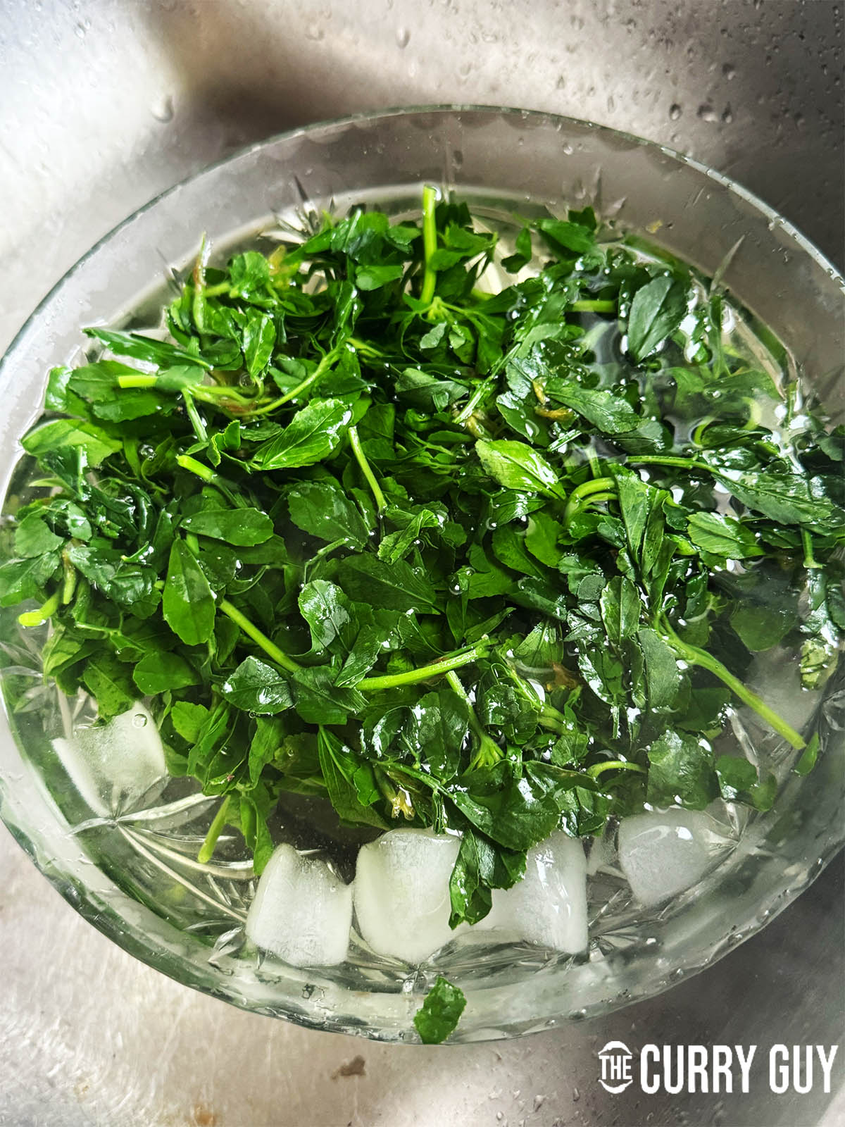 Blanched methi leaves soaking in a bowl of ice water.