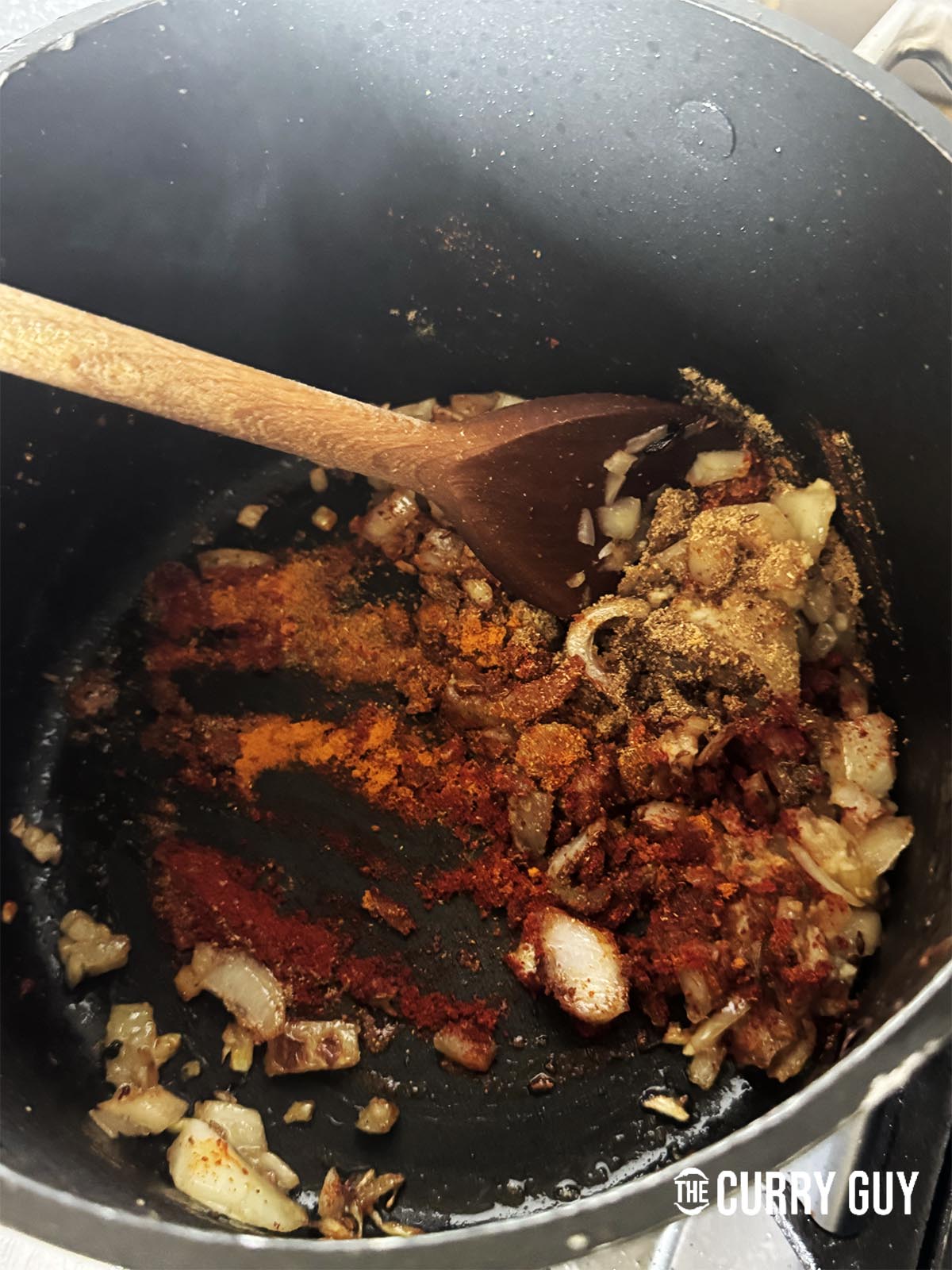 Adding garlic and ginger paste and ground spices to the frying onions in the pot.