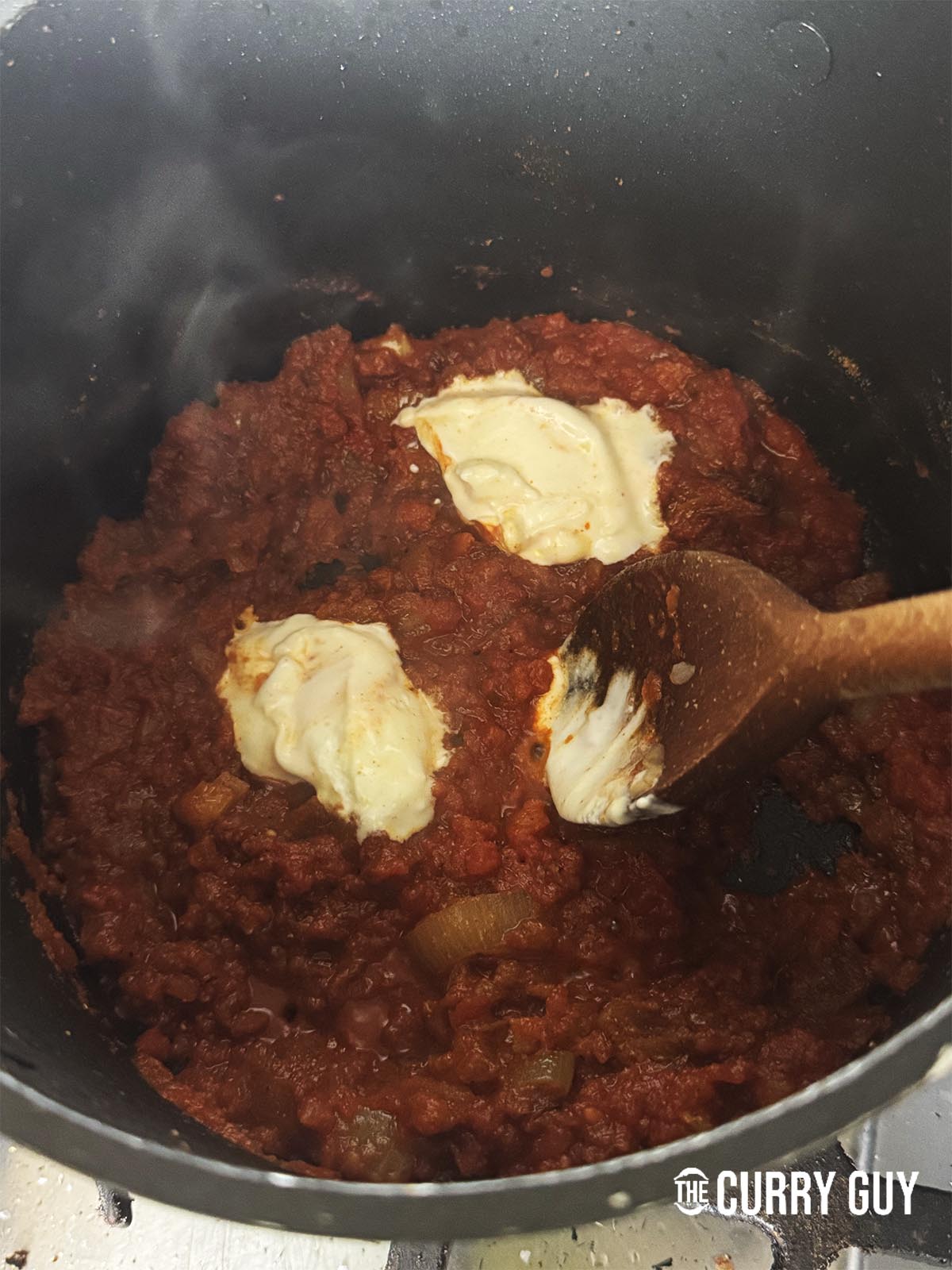 Adding yoghurt to the simmering tomatoes.
