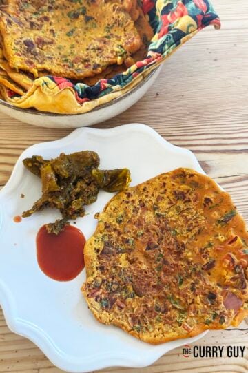 Besan chilla on a plate served with chilli pickle and hot sauce.