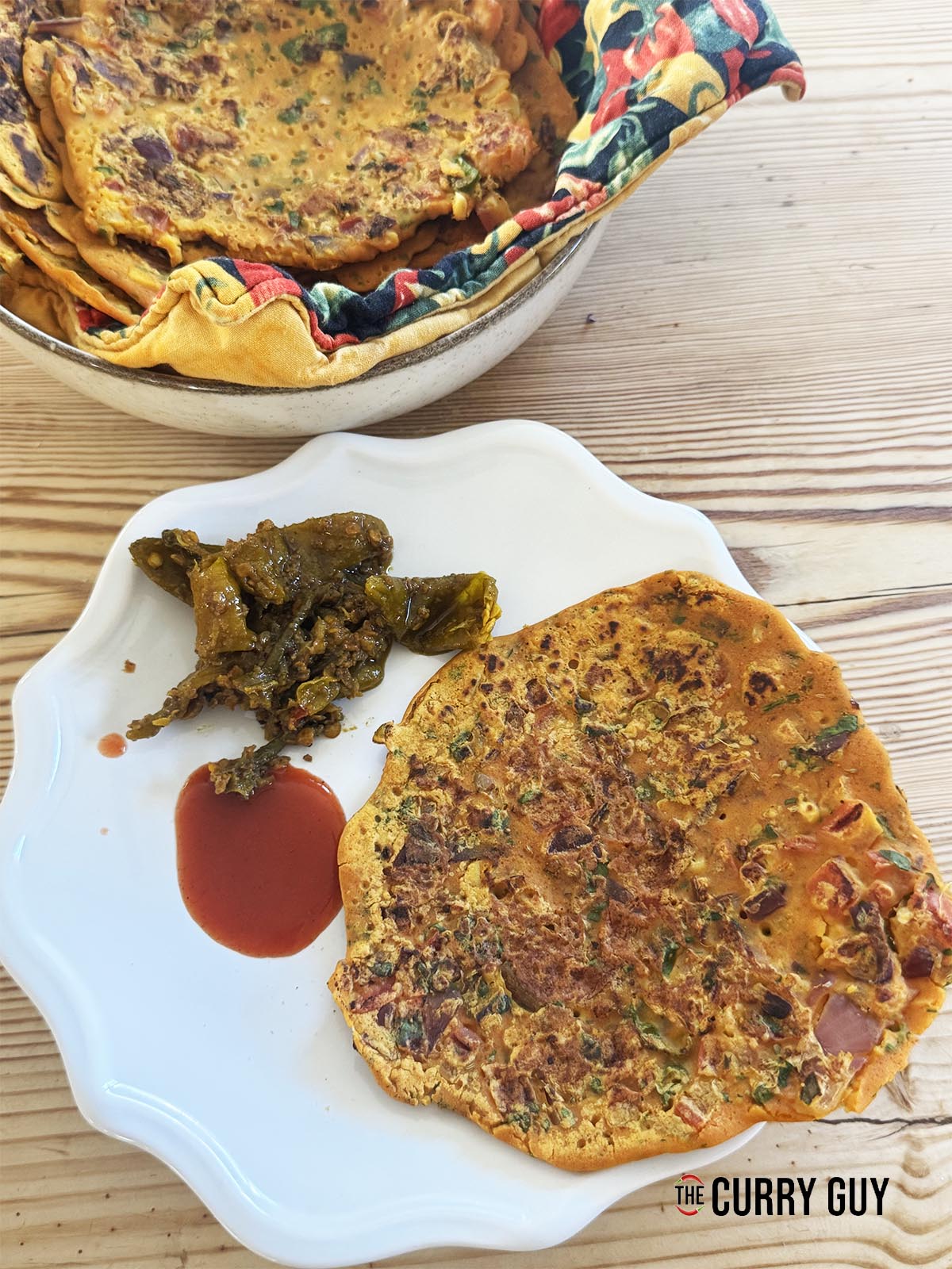 Besan chilla on a plate served with chilli pickle and hot sauce.